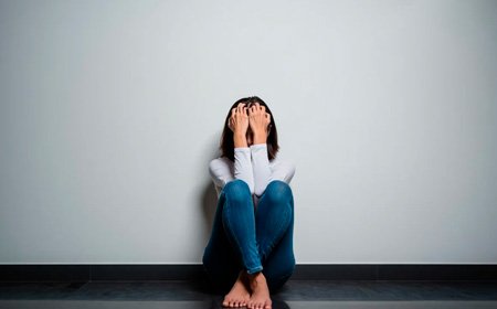 Девушка сидит на полу, закрыв лицо руками
